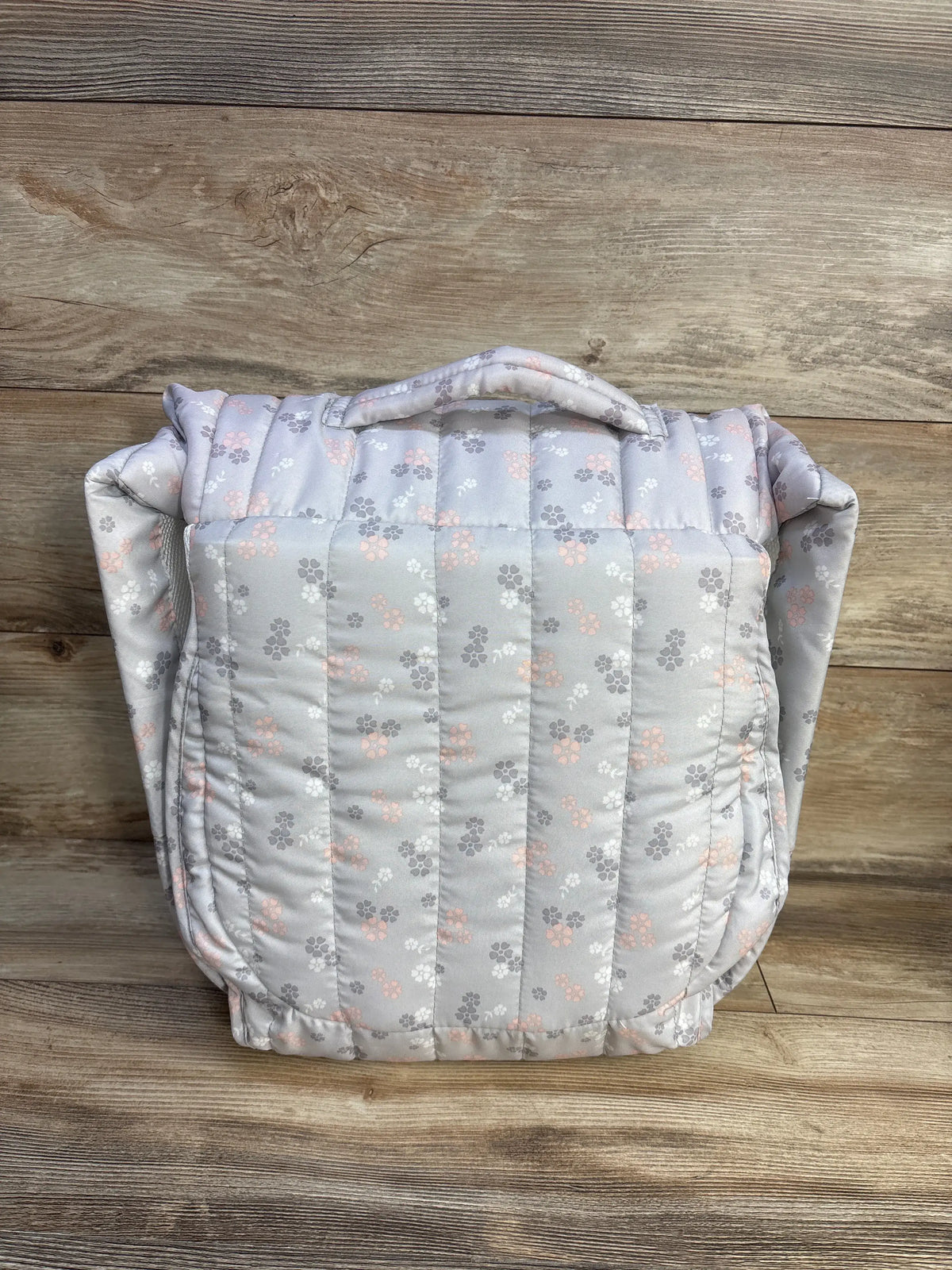 Front view of Snuggle Nest portable infant lounger folded with quilted gray fabric with pink flowers and handle on wood