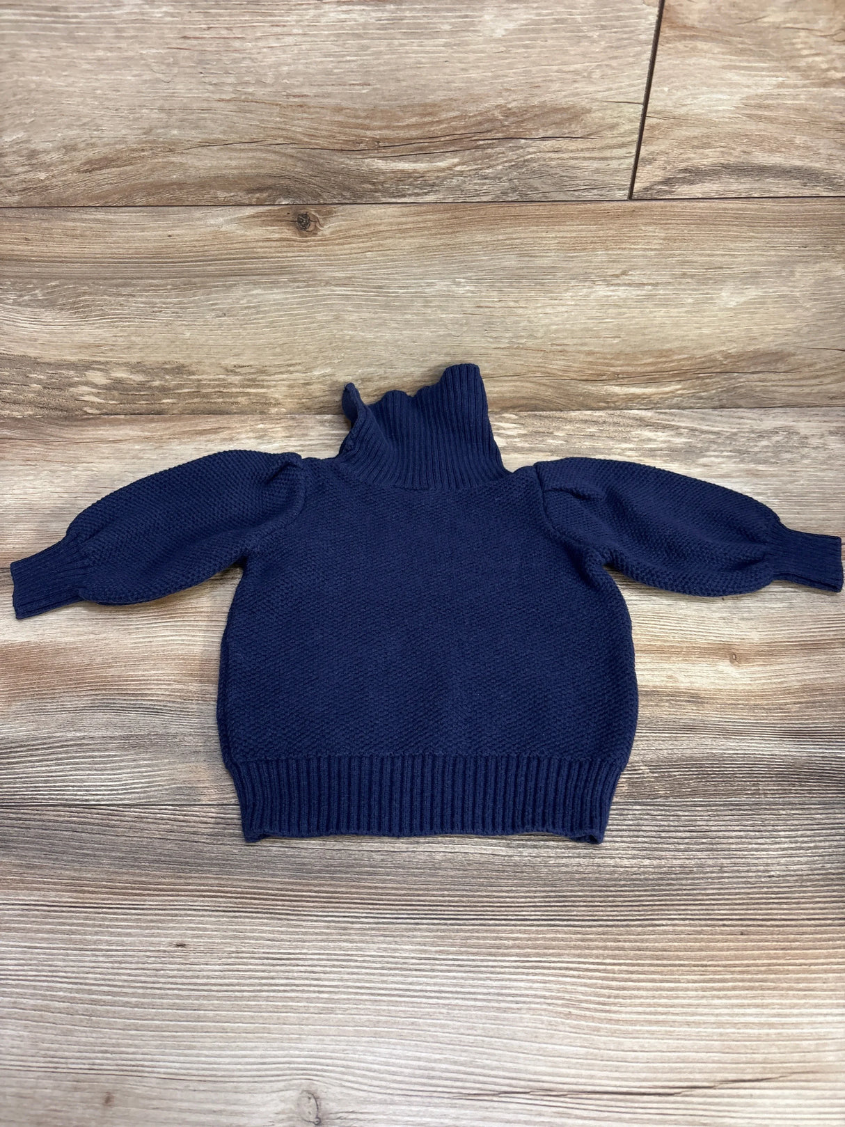 Flat lay of navy toddler turtleneck sweater size 2T with ribbed funnel neck, puff sleeves and ribbed hem on wood background