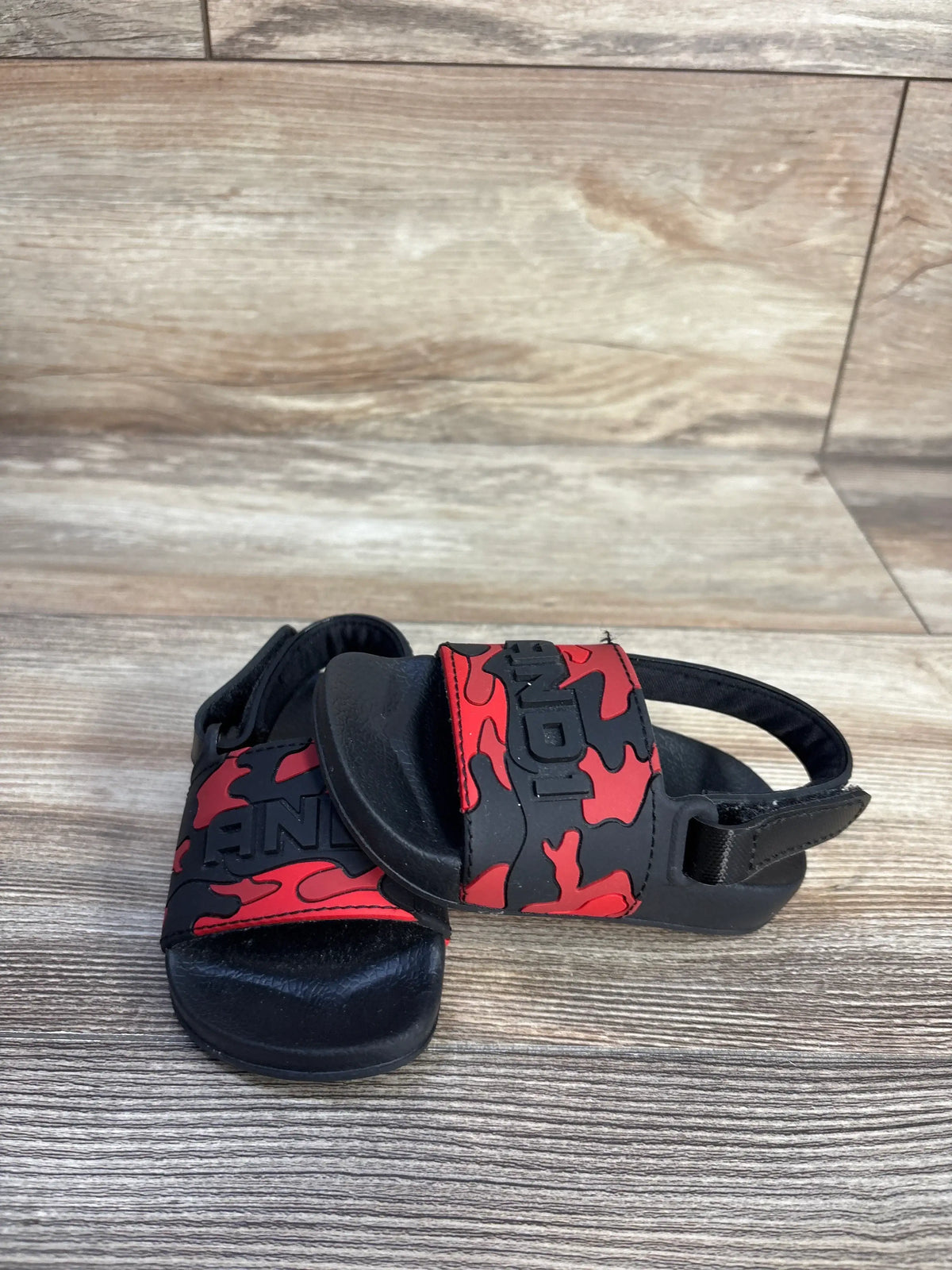 Front view of And1 camo slide sandals in red showcasing open toes and black soles with a wood-look background