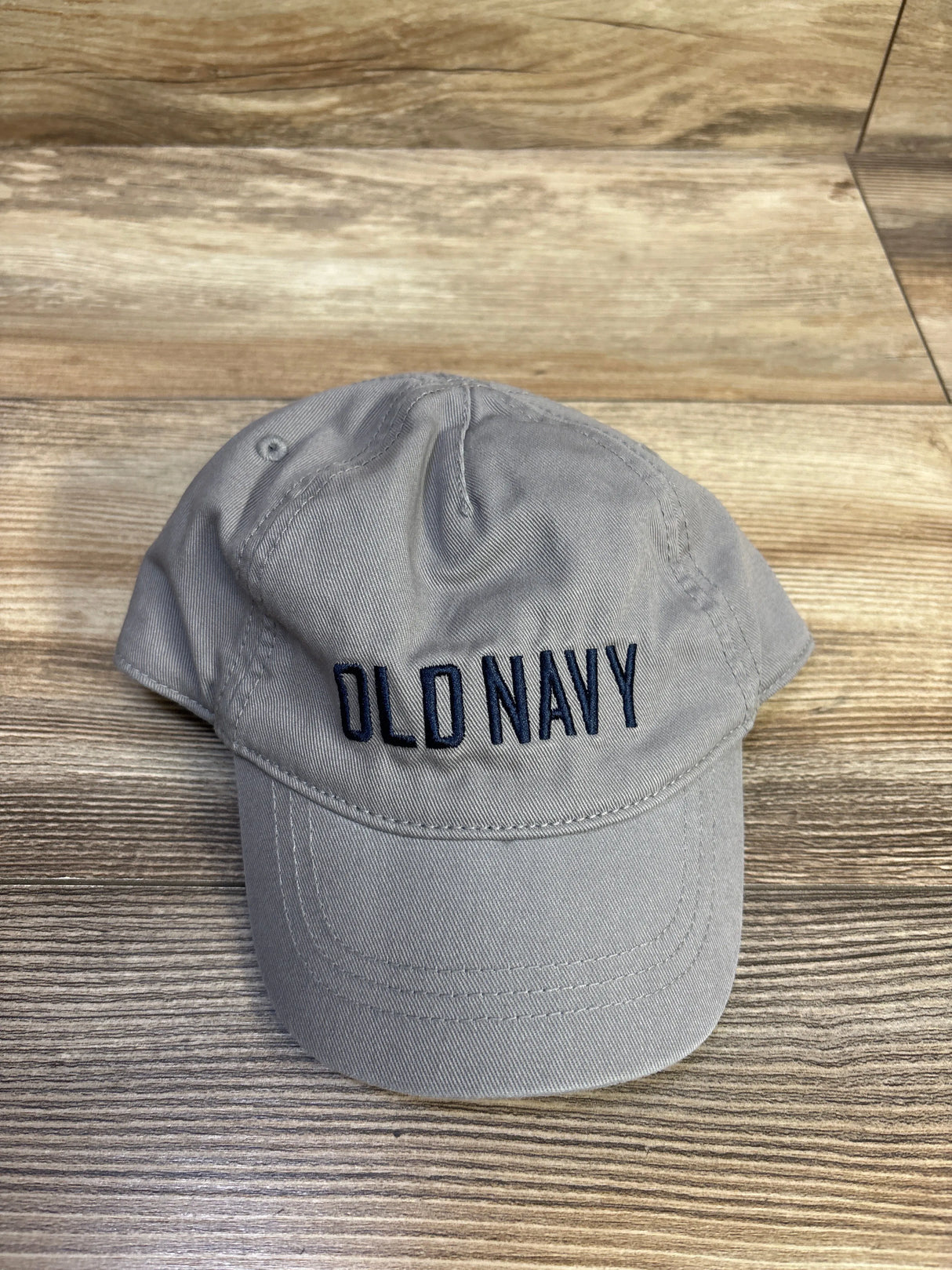 Front view of toddler baseball cap showcasing navy embroidered OLD NAVY logo on grey fabric with wood background