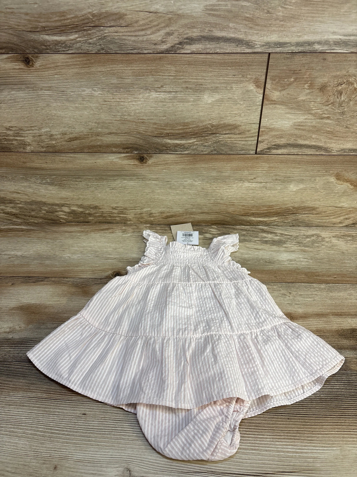 Pink striped baby dress with ruffled sleeves and tiered skirt on wooden floor