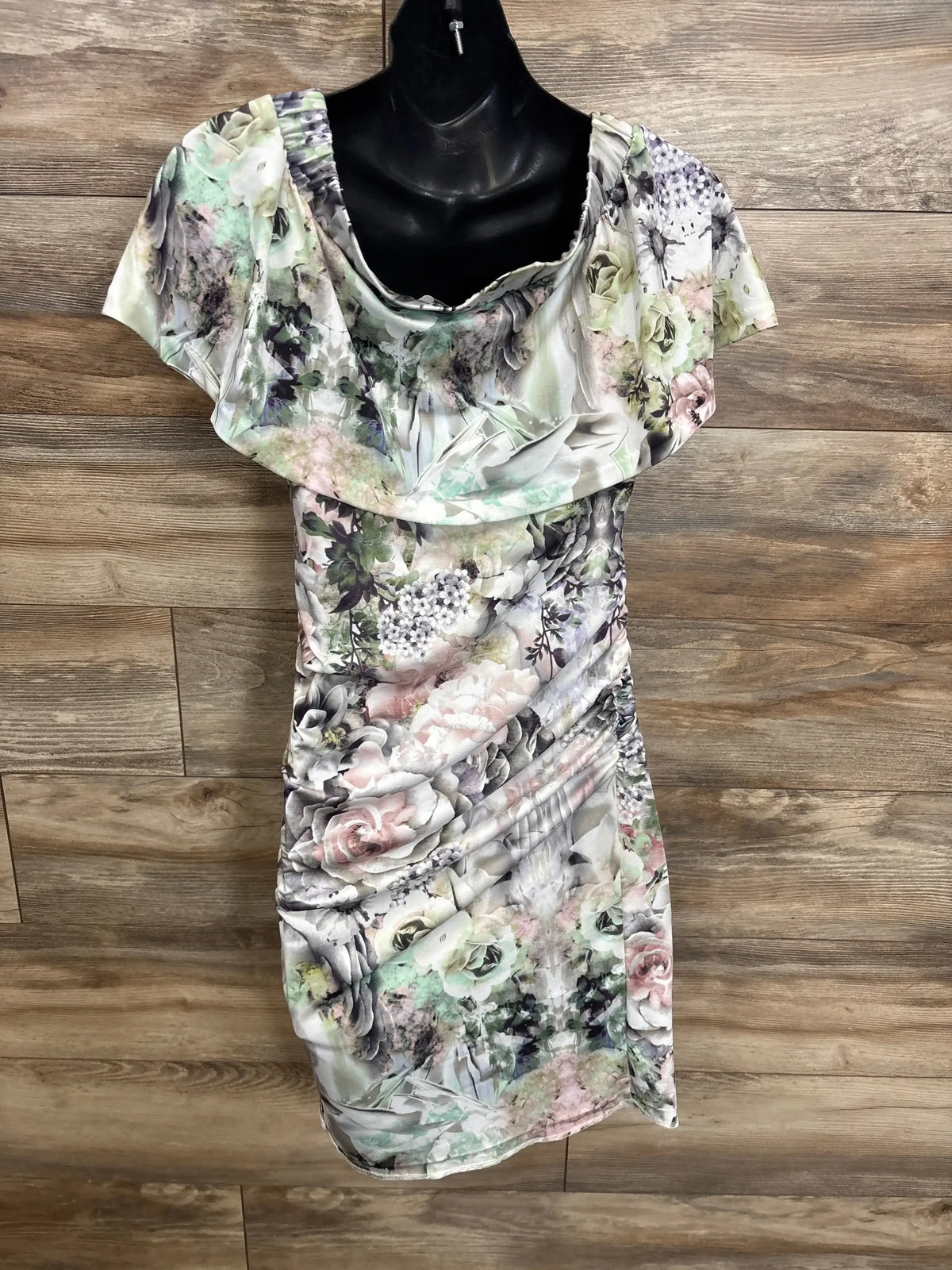Front of white Ripe Maternity off-the-shoulder floral dress showing ruffle neckline and side ruching on wood background