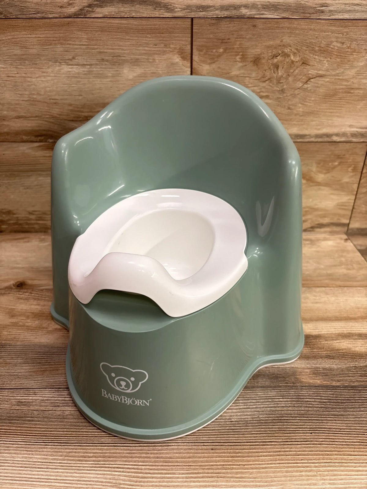 Front view of BabyBjorn Potty Chair in green showcasing its white inner seat with a wood background