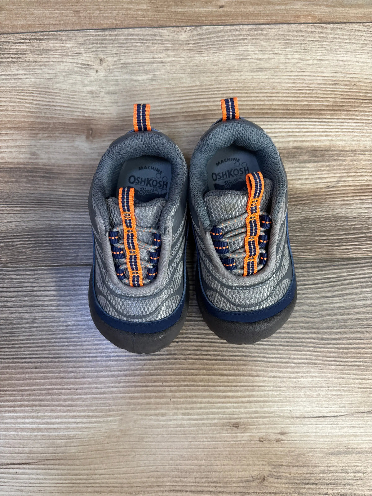 Top view of grey Oshkosh Gianni bump toe sneakers with reinforced toe protection and orange accents on wood