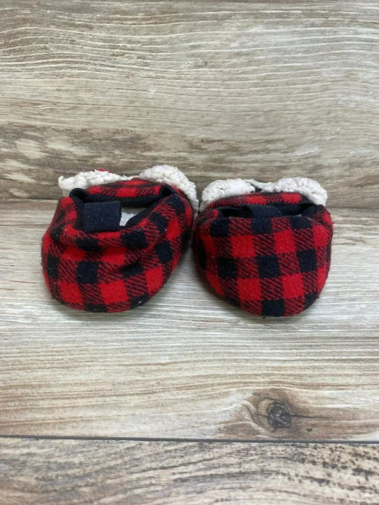 Front view of baby bear slippers (size 1C) showing red and black buffalo plaid and white sherpa cuff on wood background