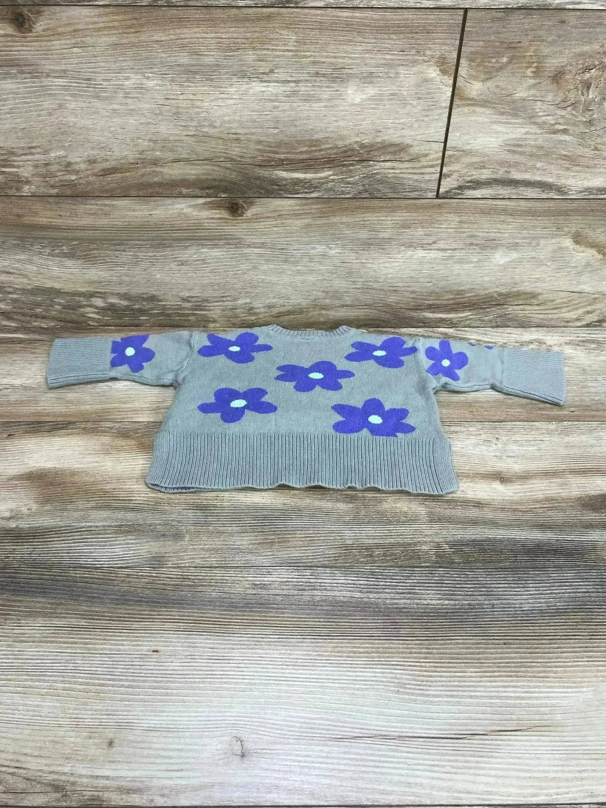 Front flat lay of Baby Gap floral knit sweater showing purple flower motifs and ribbed cuffs on light wood background