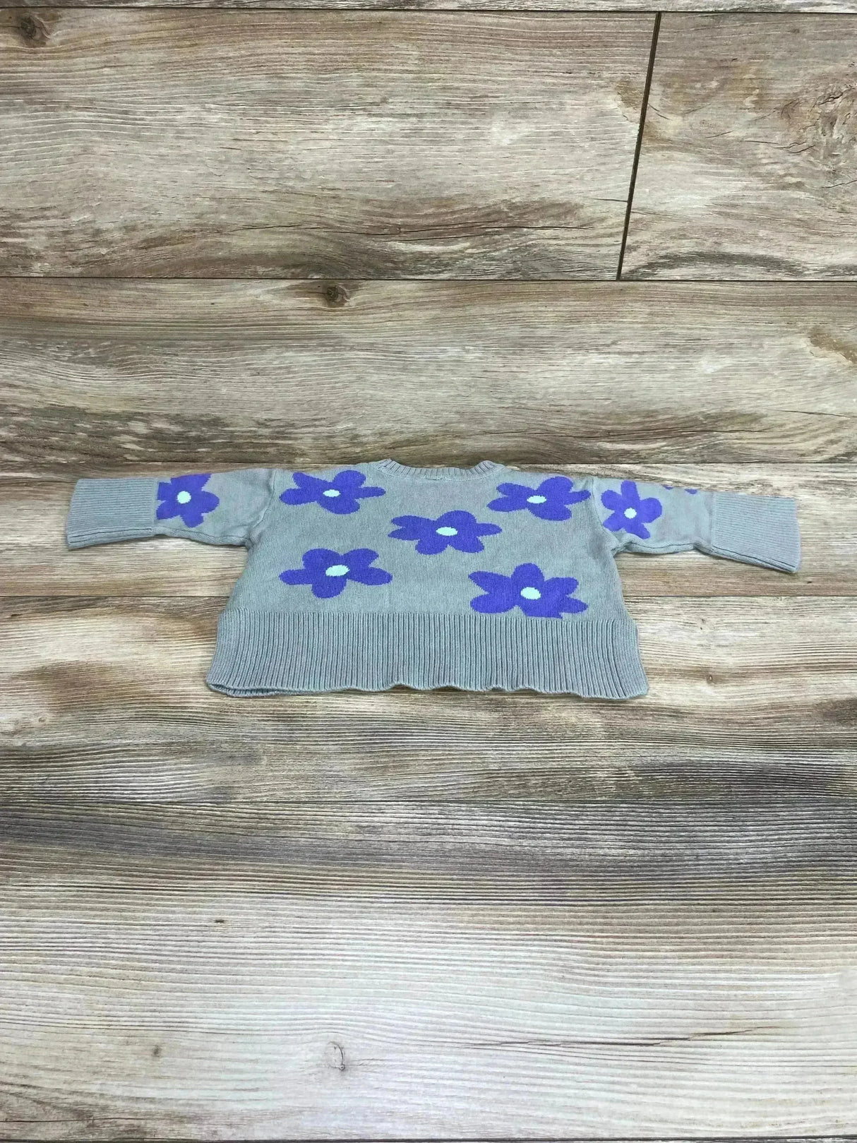 Flat lay of Baby Gap split-hem knit sweater, 12-18 months, showcasing purple flower motifs and ribbed cuffs on light wood background