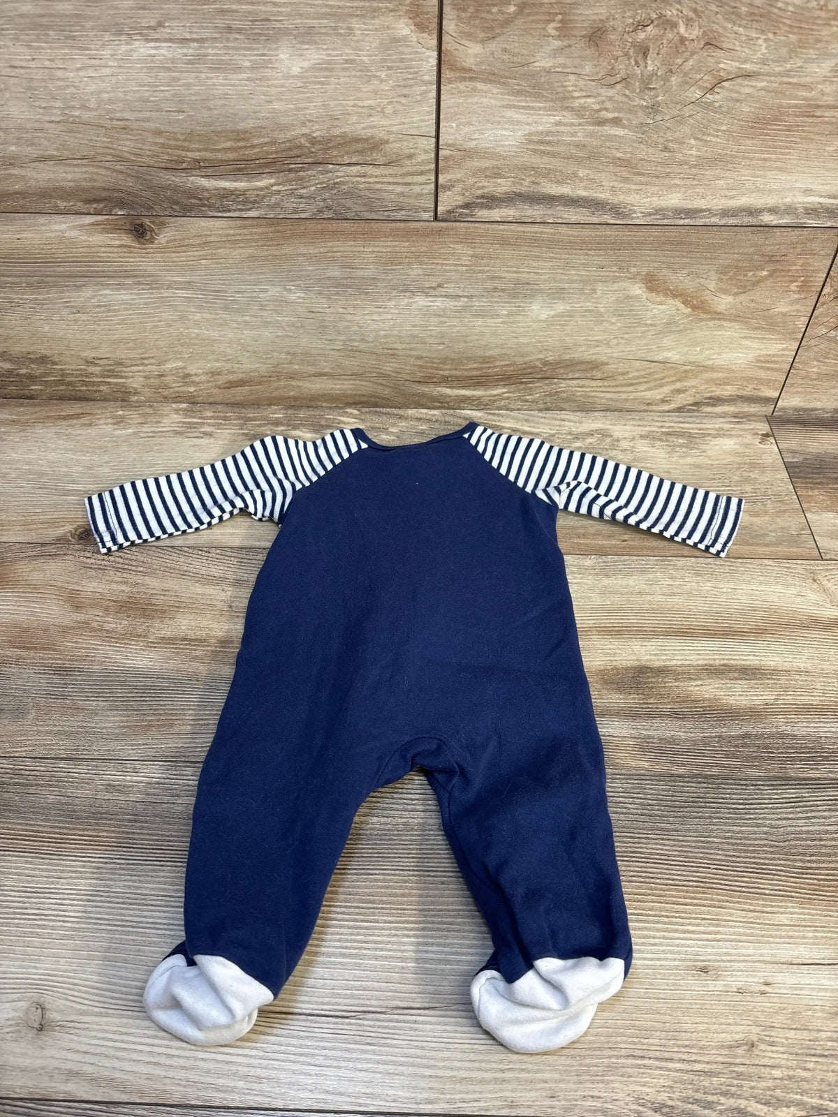 Navy blue baby onesie with striped sleeves and footed cuffs on wood floor