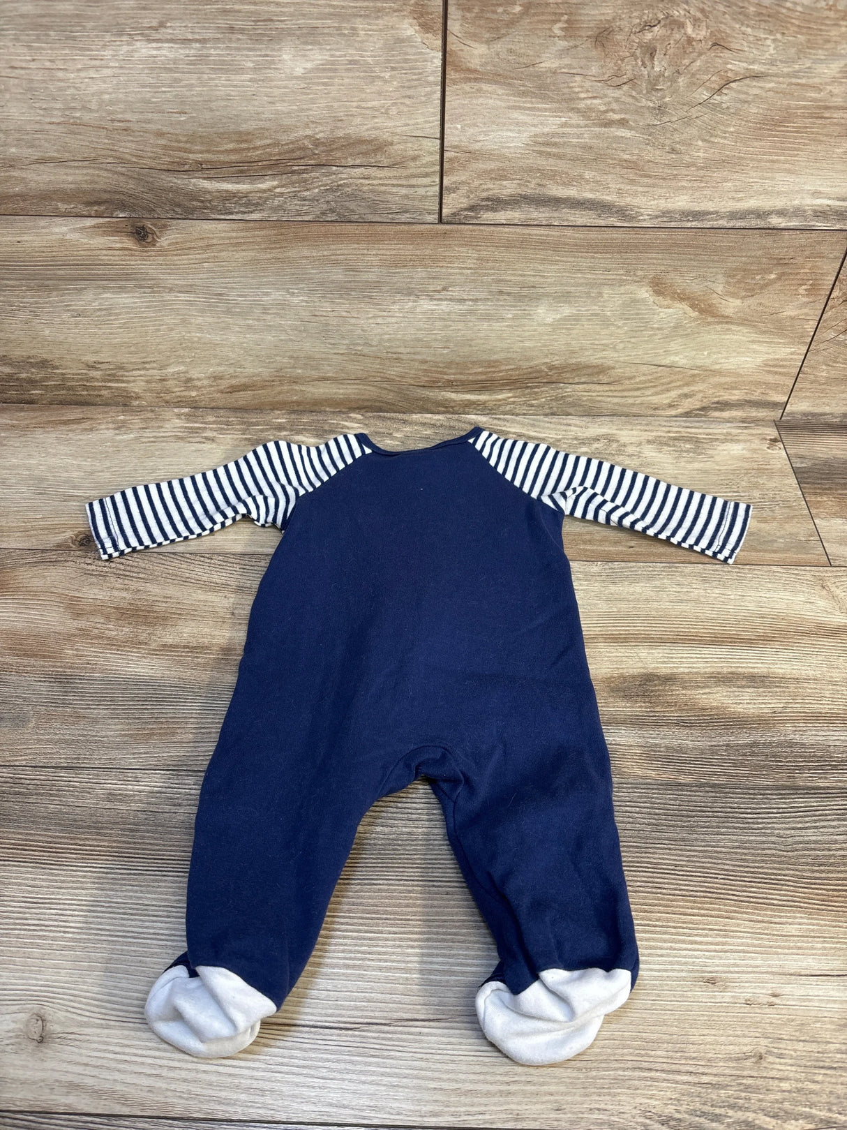 Navy blue baby onesie with striped sleeves and footed cuffs on wood floor