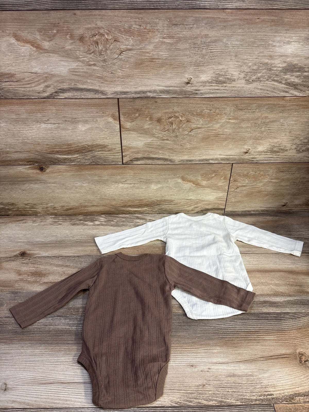 Top view of Kyle + Deena two-pack kimono ribbed bodysuits in brown and white on a wood background