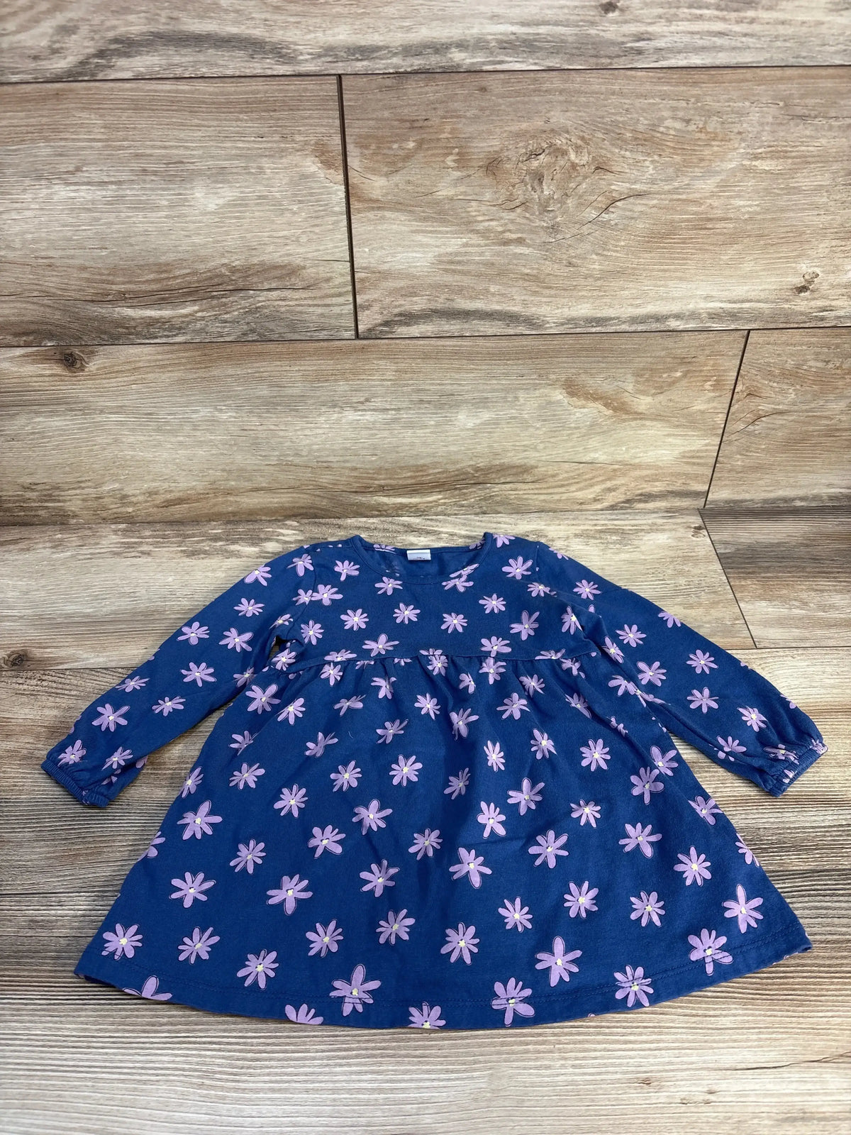 Long sleeve blue girls dress with pink floral print, laid flat on wooden background