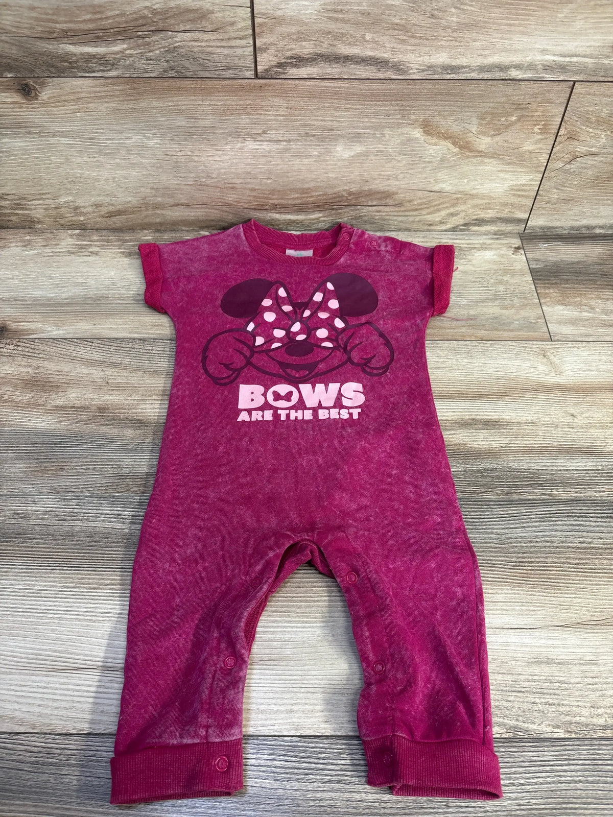 Front flat-lay of magenta Minnie Mouse jumpsuit 12mo with bow graphic, BOWS ARE THE BEST slogan and snap leg closures