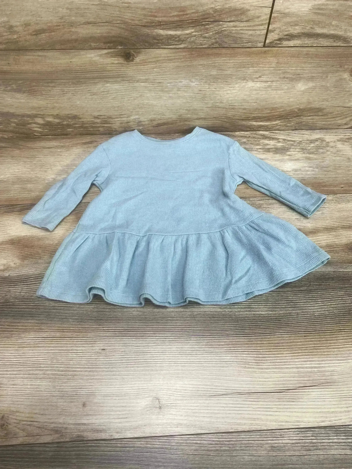 Flat lay of blue Old Navy toddler peplum thermal shirt showing long sleeves and gathered ruffle hem on wood floor