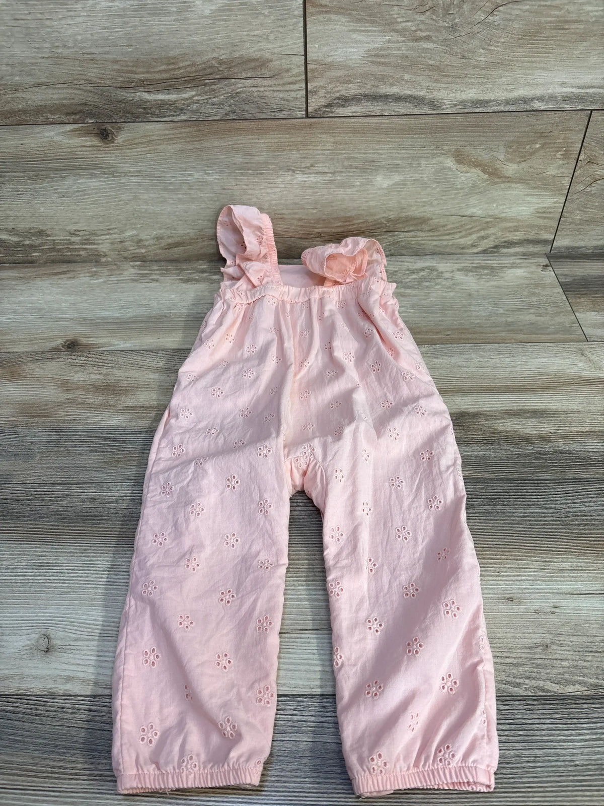 Front view of Carter’s pink eyelet sleeveless jumpsuit in size 18m showcasing eyelet details on a wood-look background