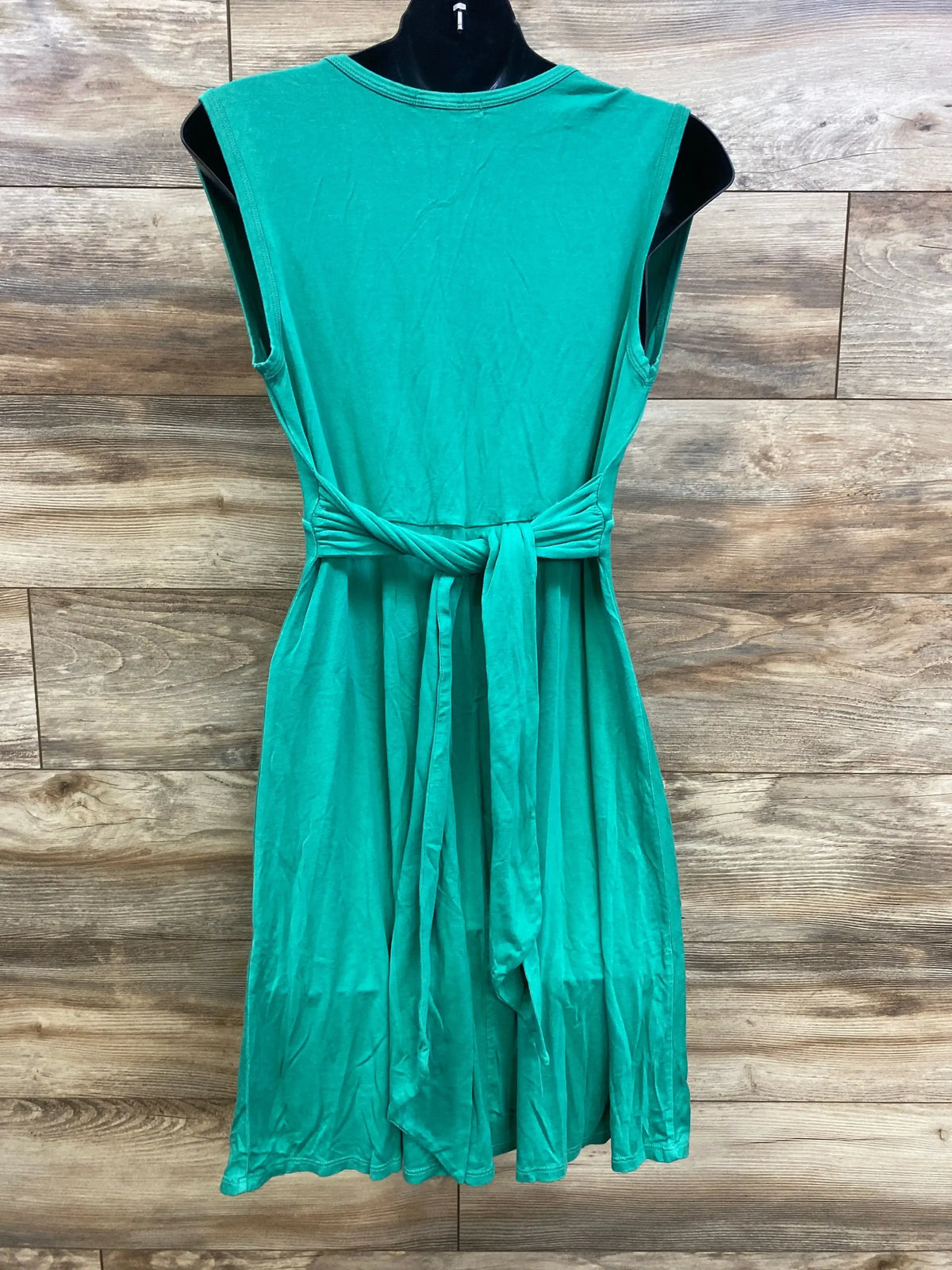 Back view of Maternal America sleeveless green maternity dress with tied waist belt and full skirt on wood plank background