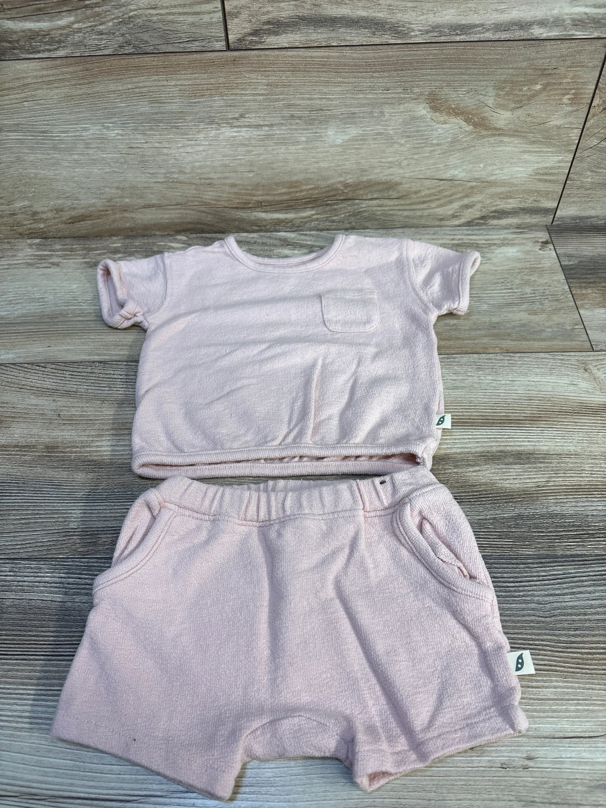 Flat lay of pink Easy Peasy short-sleeve shirt and elastic-waist shorts showing terry texture, chest pocket, and side tags