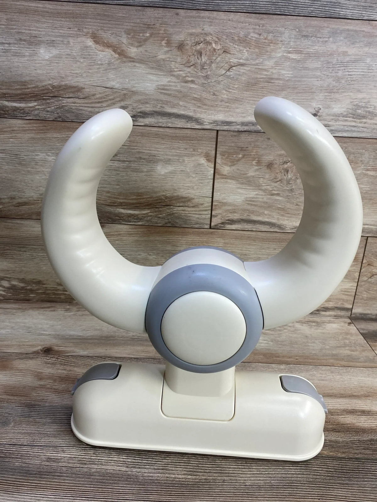 Close-up front view of NEW IvyWind Wall-Mounted Baby Shower Stand in white with curved arched arms and grey hub on a wood plank background