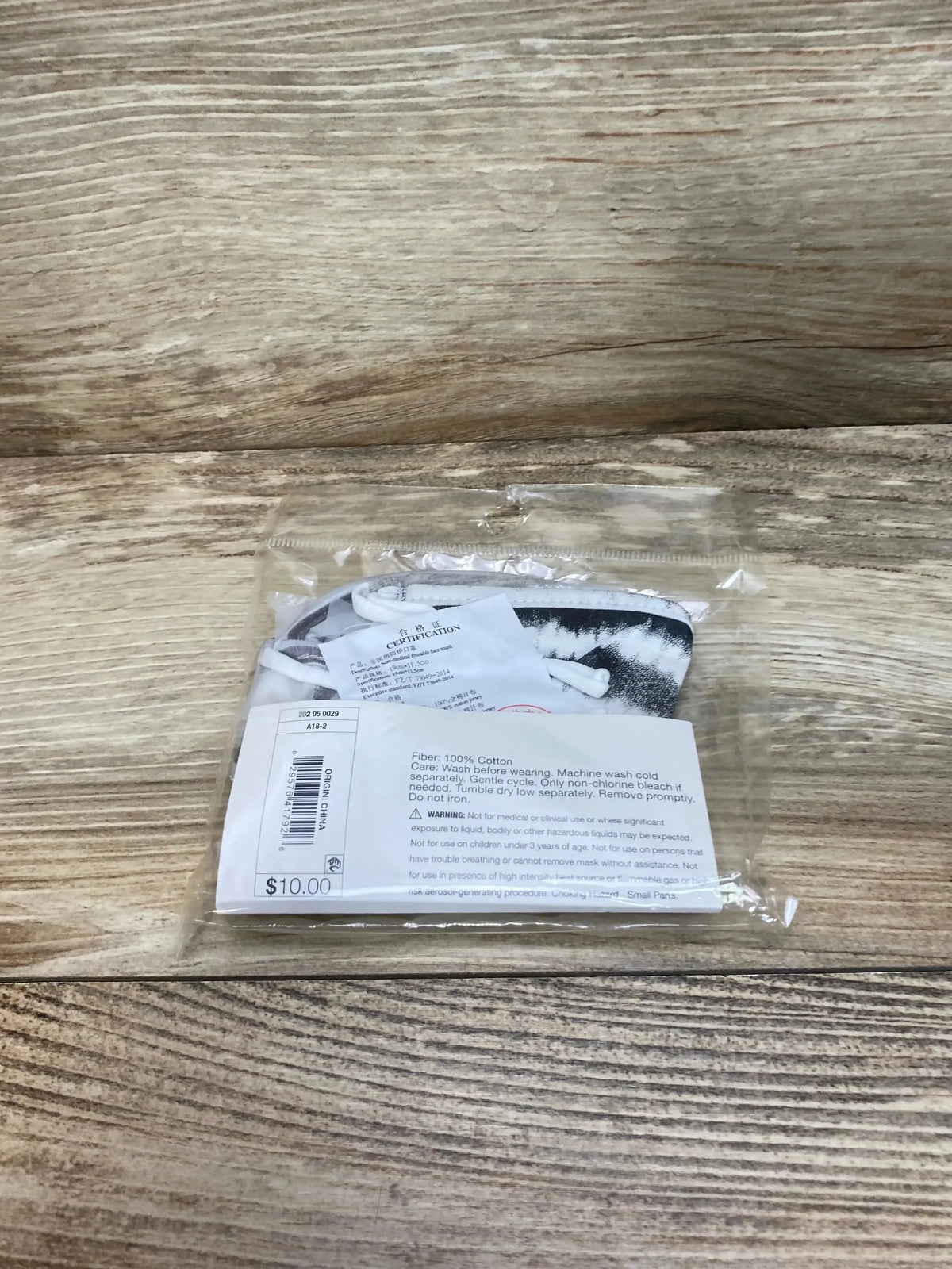 Front view of pack of three grey kids' reusable cotton face masks with adjustable ear loops in clear plastic bag on wooden background