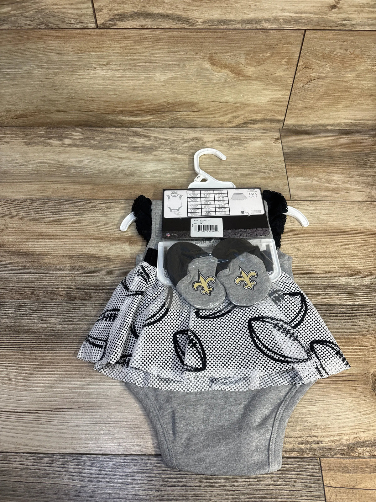 Flat lay of New Orleans Saints three-piece creeper set showcasing gray bodysuit, football-print skirt, and fleur-de-lis booties
