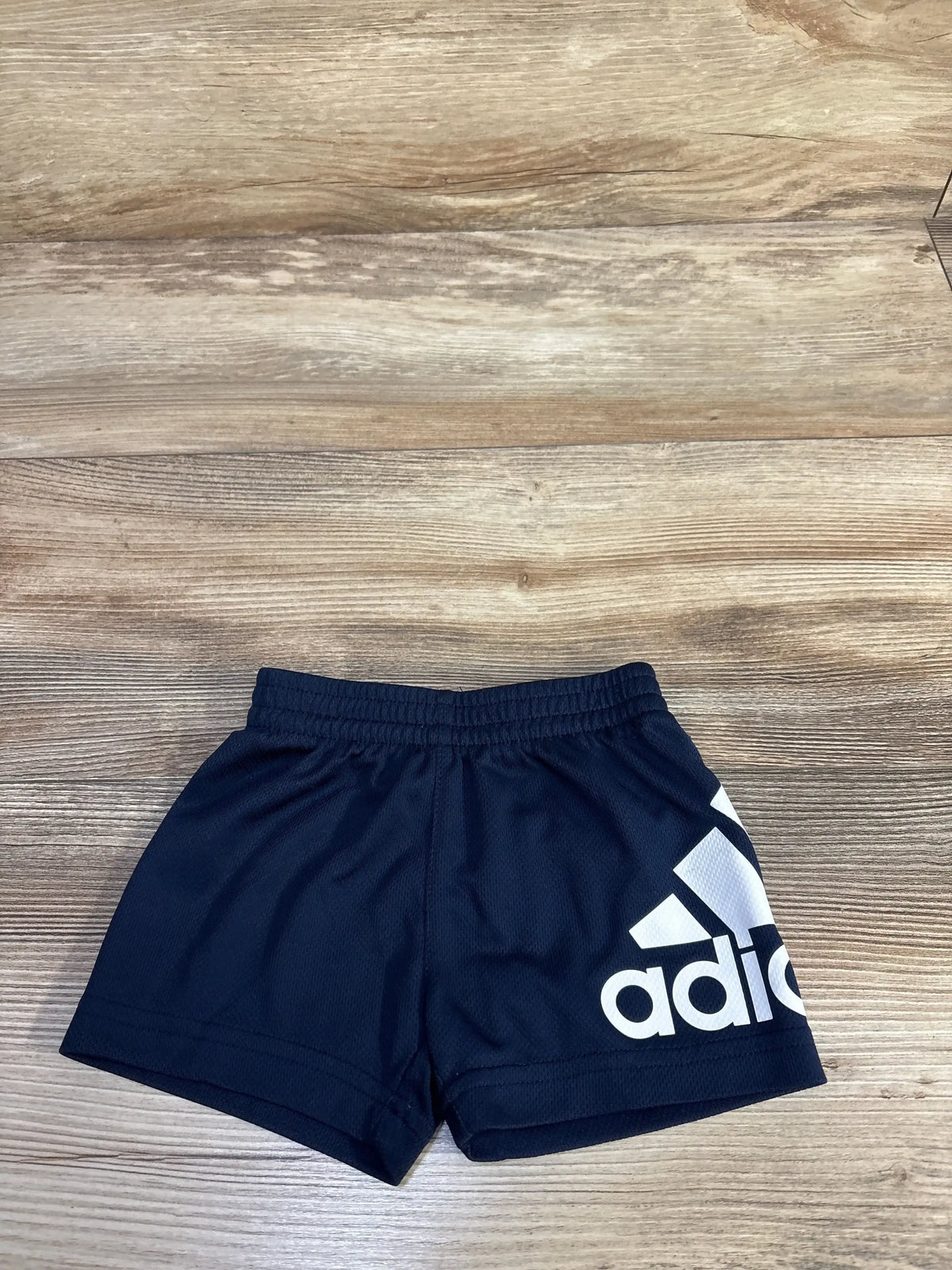 Top-down view of navy Adidas baby mesh shorts showcasing elastic waistband and large white Adidas logo on wood floor