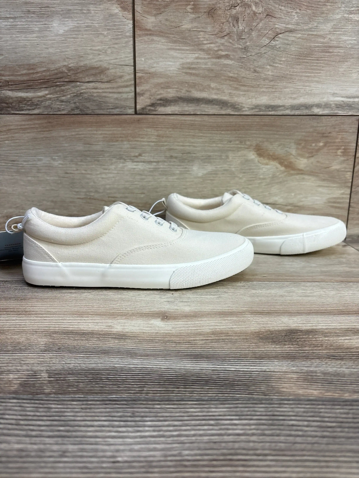 Side view of NEW Cat and Jack Tyler Slip-On Sneakers in off-white sz 4Y showcasing canvas upper and white rubber soles on wood plank background