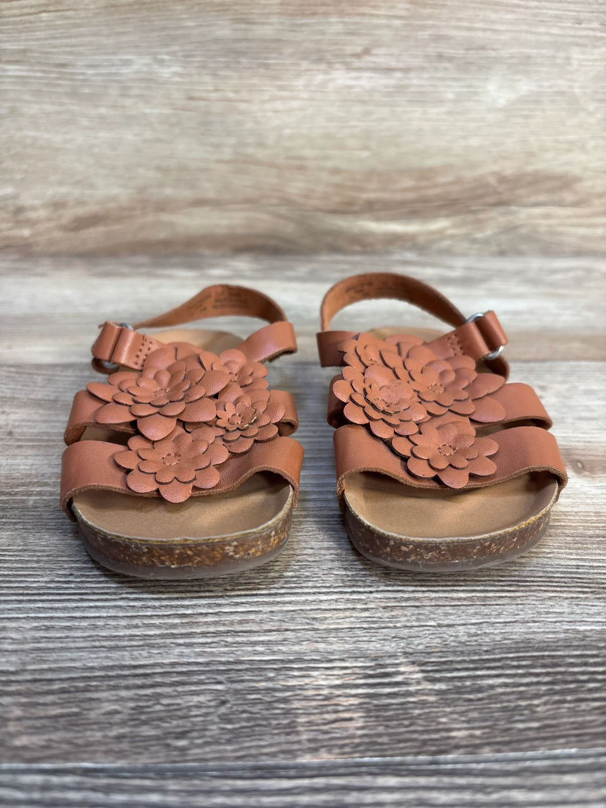 Brown toddler sandals with floral design on cork soles, kids footwear on wood background