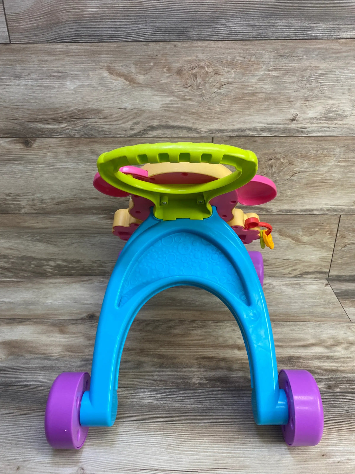 Front view of Fisher-Price Puppy walker showing blue arched base, purple wheels, green handle, toy keys on wood floor