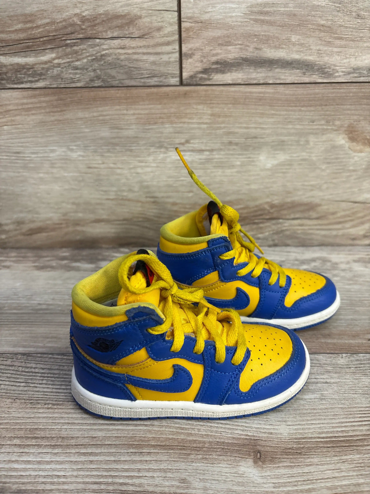 Side view of Air Jordan 1 Retro High OG TD ‘Reverse Laney’ sneakers with yellow leather uppers and blue overlays on wood grain