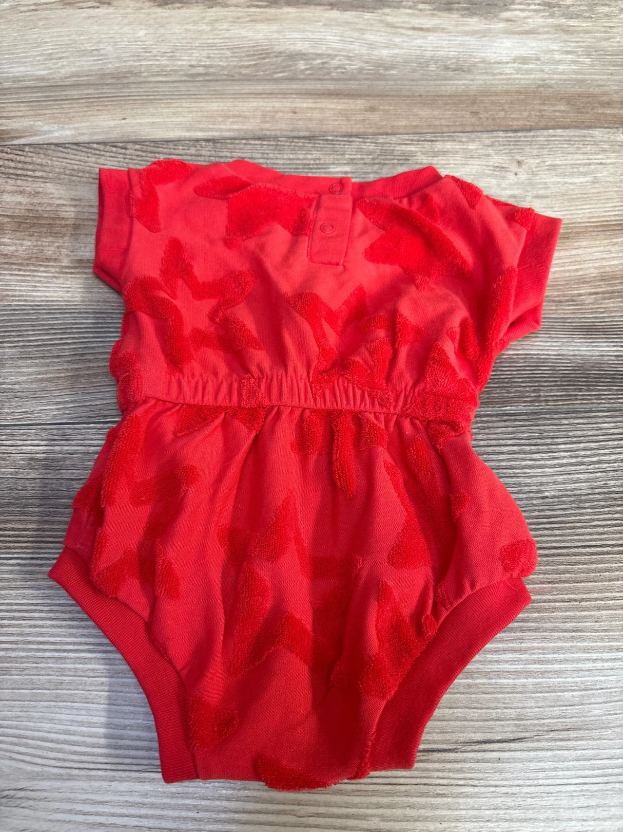 Flat lay of red Cat & Jack newborn terry star romper with textured star pattern, elastic waist, and snap closure on wood background