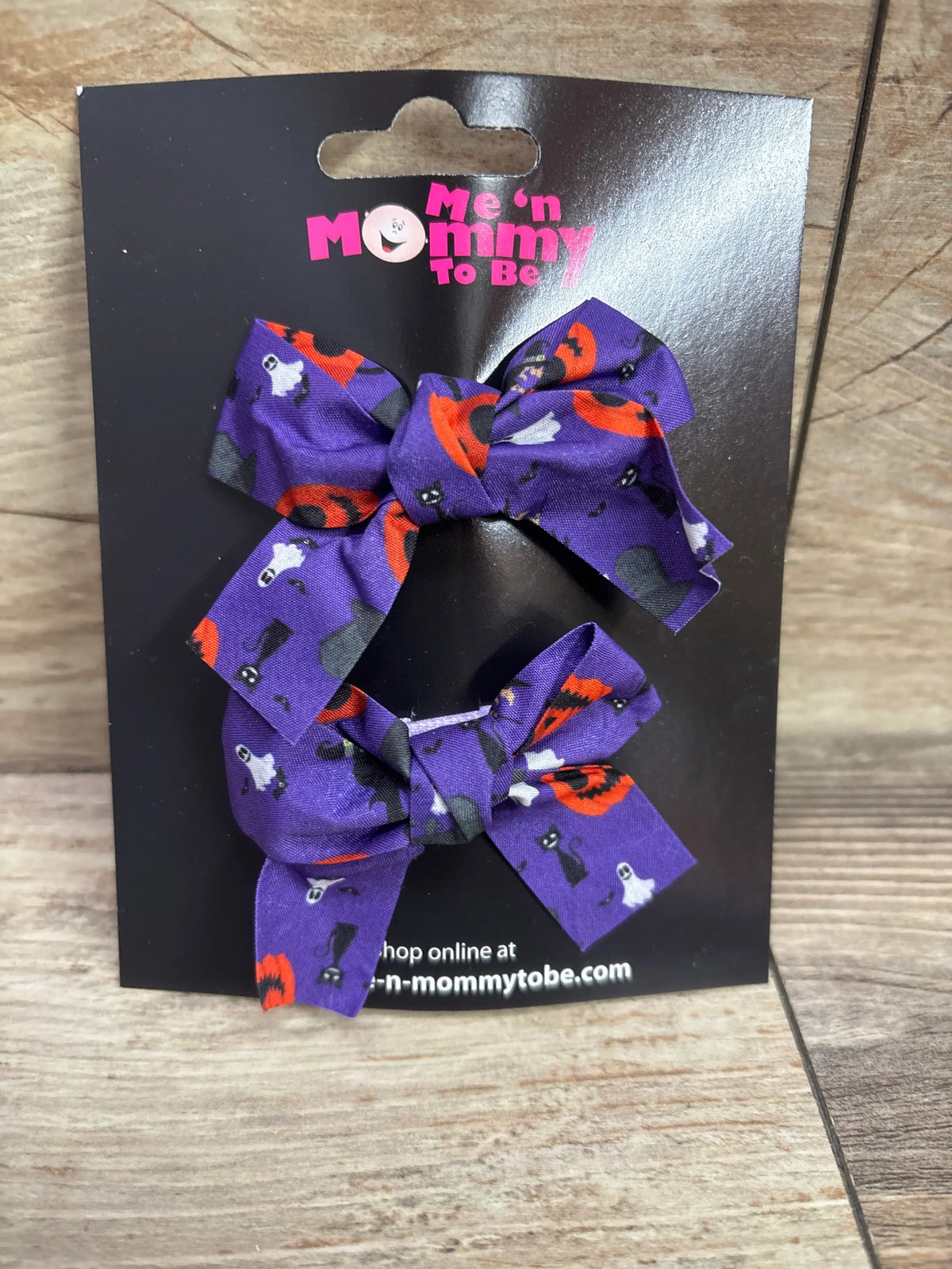 Two purple Halloween print hair bows with pumpkins and ghosts on a Me n Mommy To Be card.