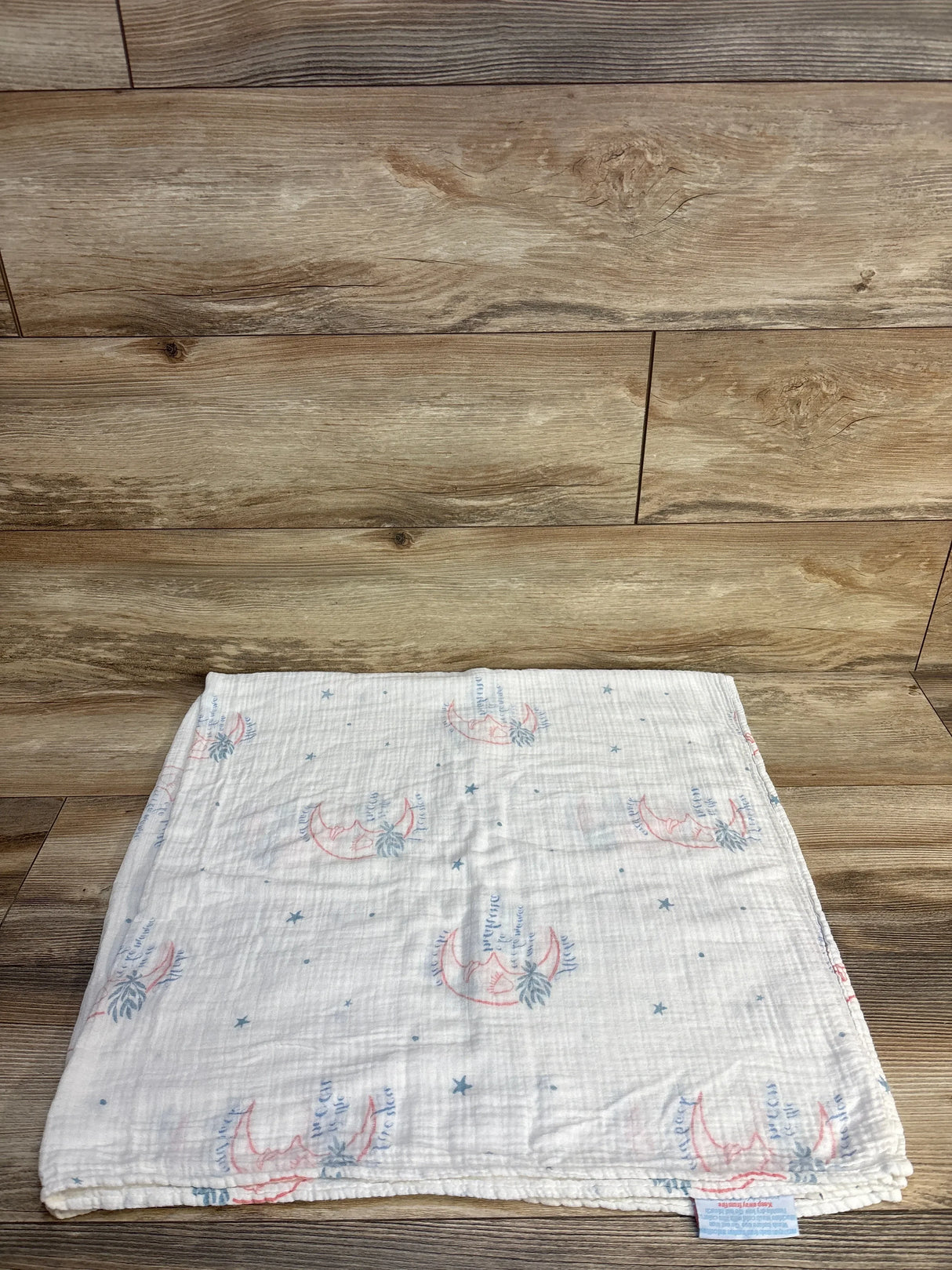 Folded muslin baby blanket with pink moon and blue feather print on wood background