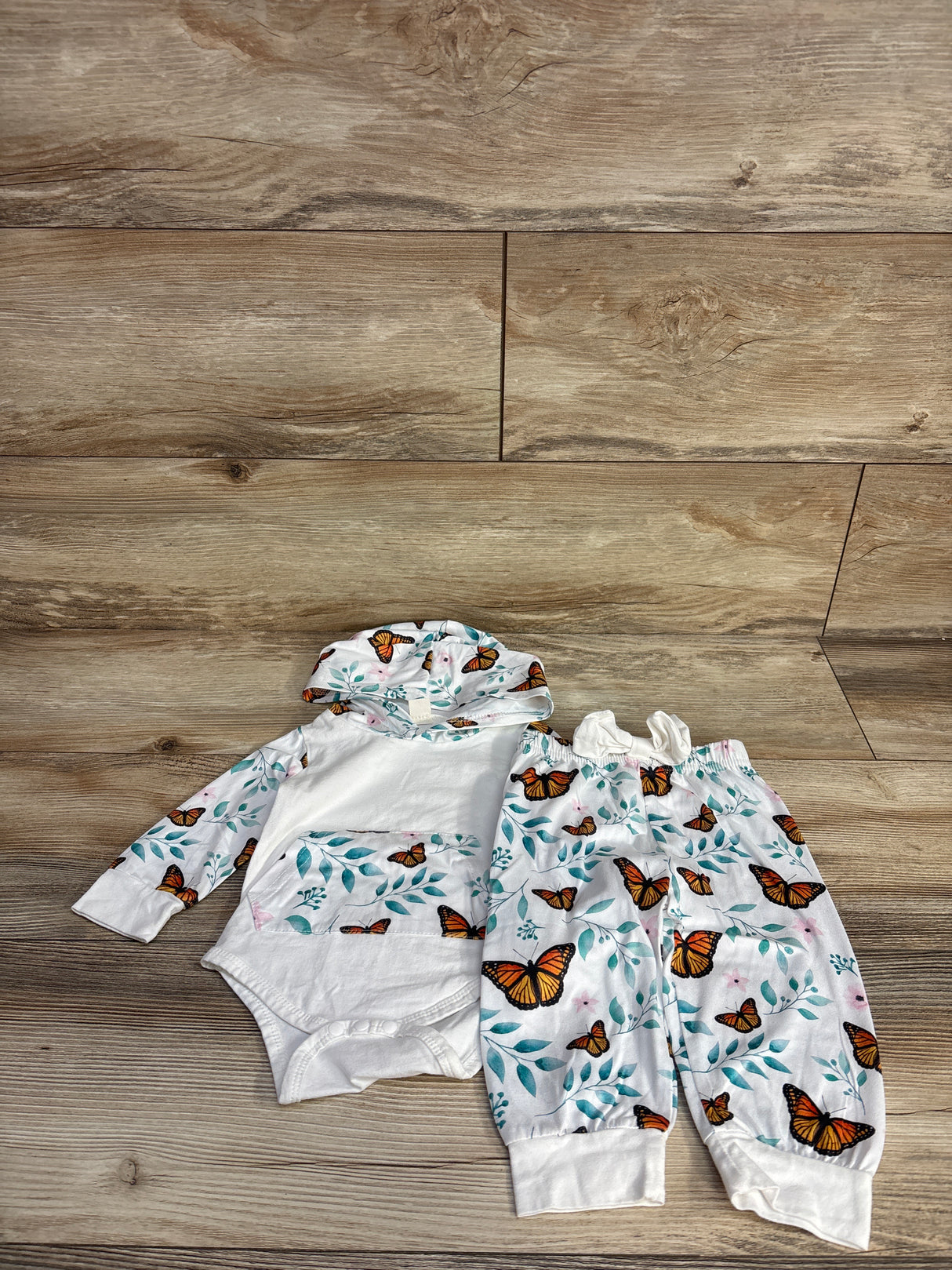 White baby hoodie and pants set with orange butterfly and teal leaf print on wood floor