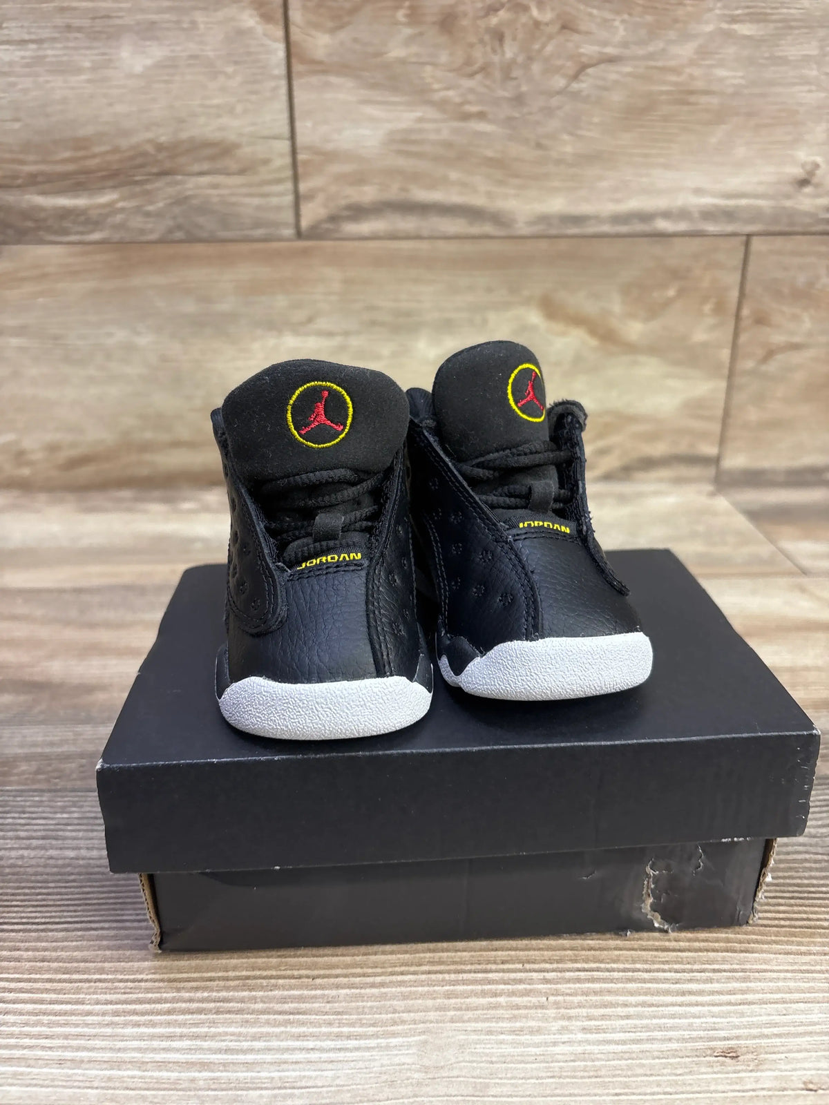 Front view of black Air Jordan 13 Retro TD Playoff sneakers showcasing white soles and red-yellow logos with black shoebox background