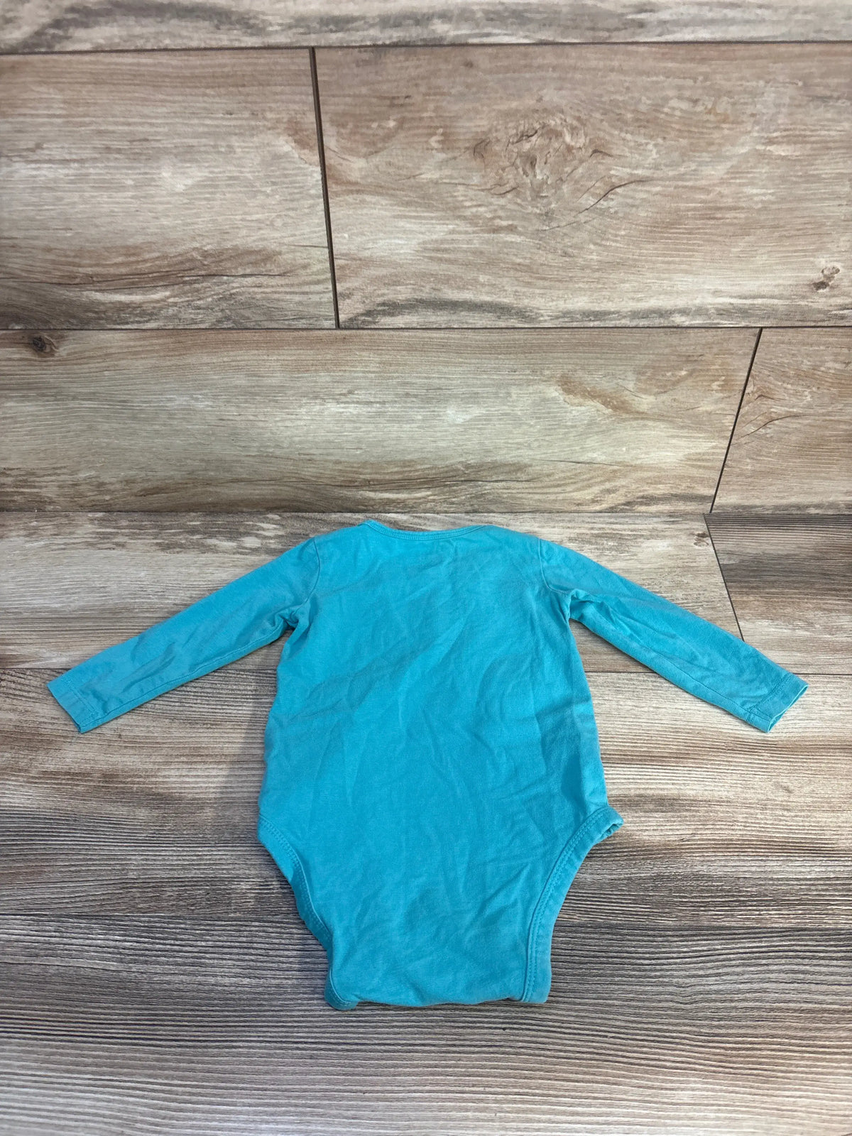 Front view of Wrangler teal long sleeve bodysuit, size 12 months, showcasing long sleeves and bodysuit bottom on a wood-patterned floor