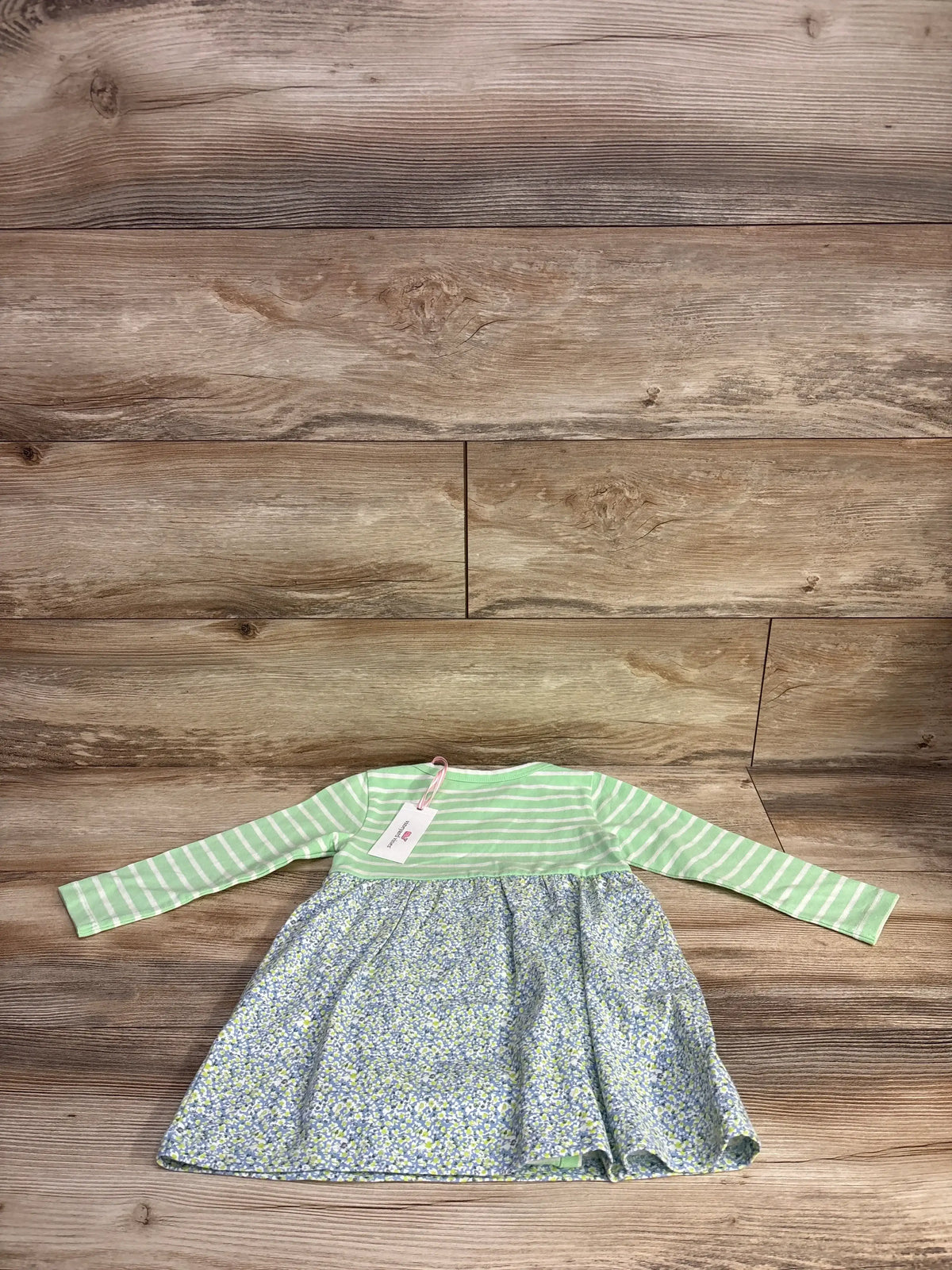 Green and white striped long-sleeve baby dress with floral skirt on wood background