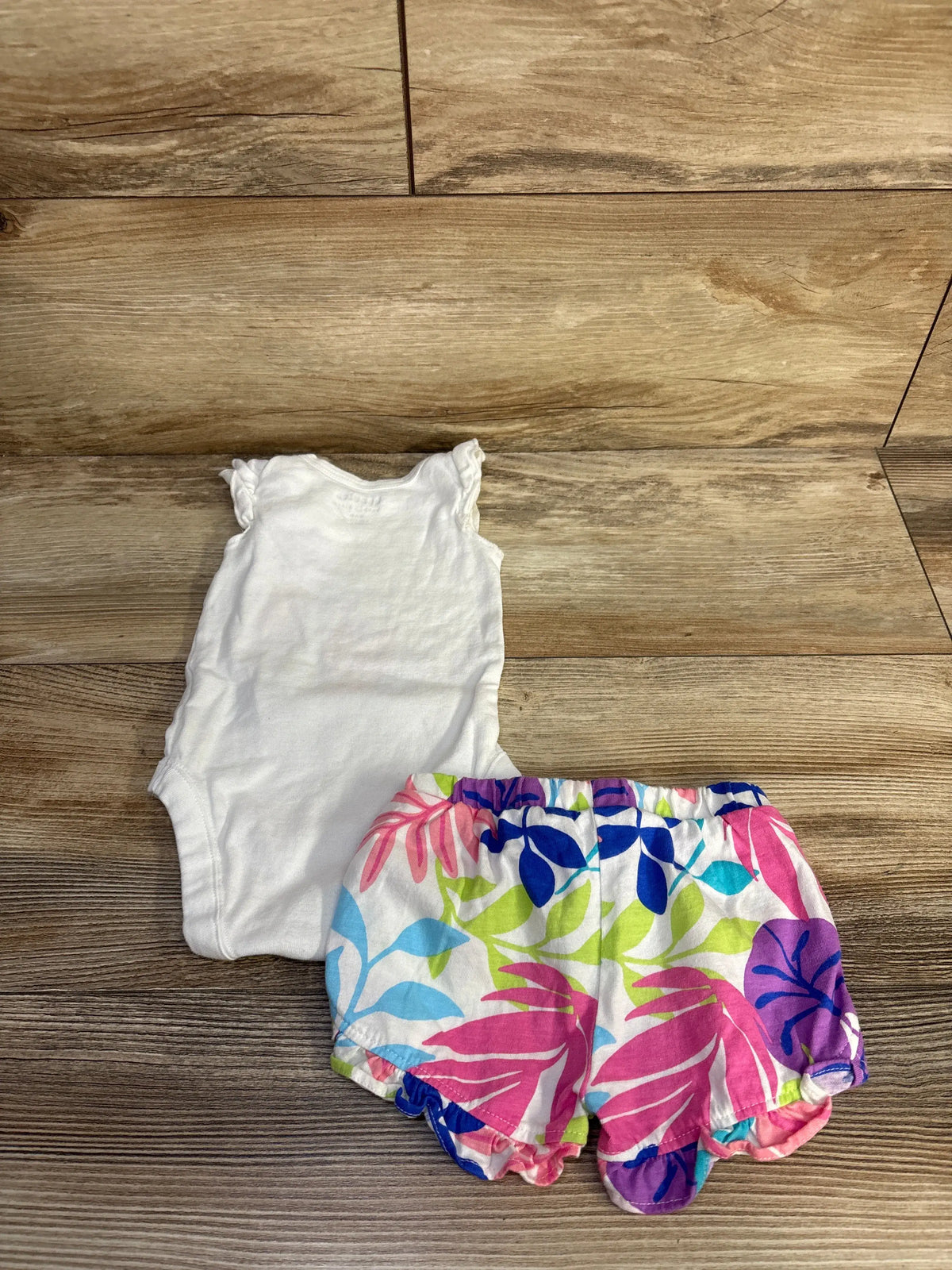 Top view of Children’s Place two-piece bodysuit and shorts set showcasing white bodysuit and colorful floral shorts on a wood floor