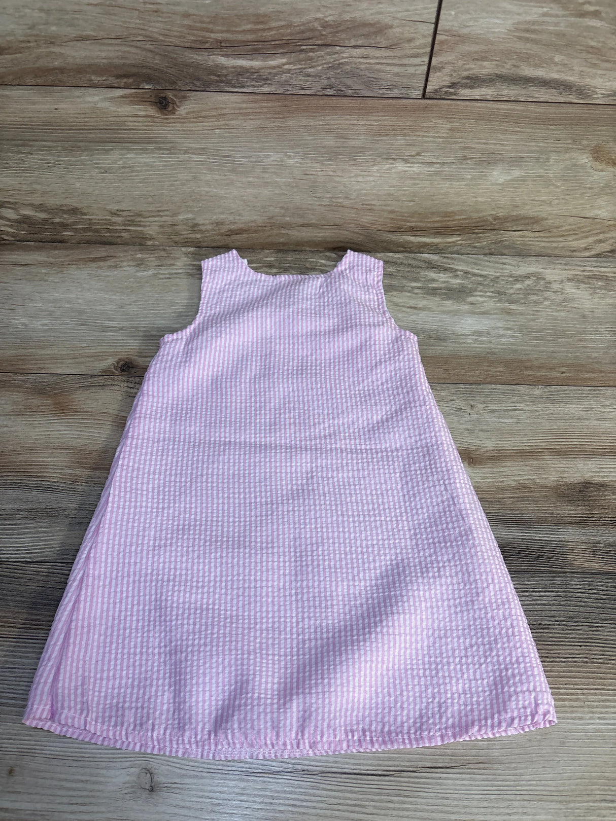 Pink and white striped sleeveless baby dress on wood floor