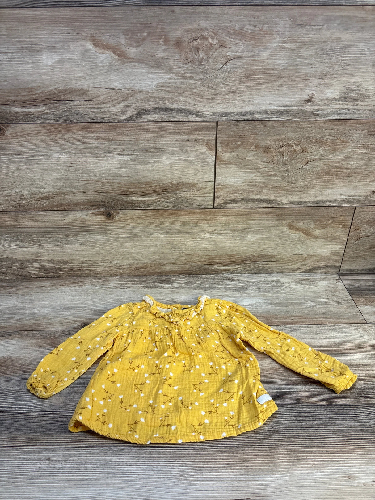 Yellow long sleeve baby top with white floral print on wood background