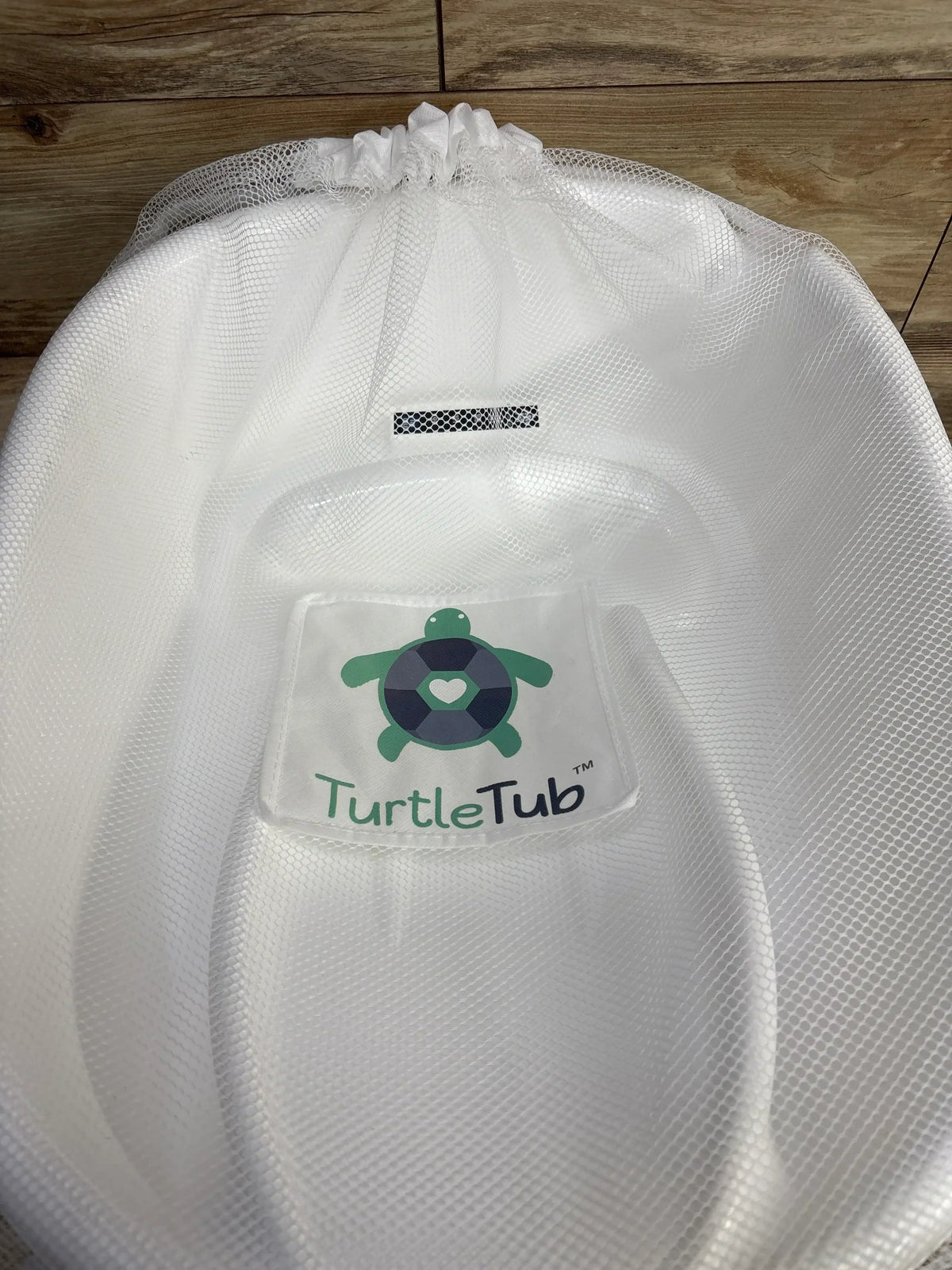 White TurtleTub mesh baby bath seat with turtle logo on wooden floor background