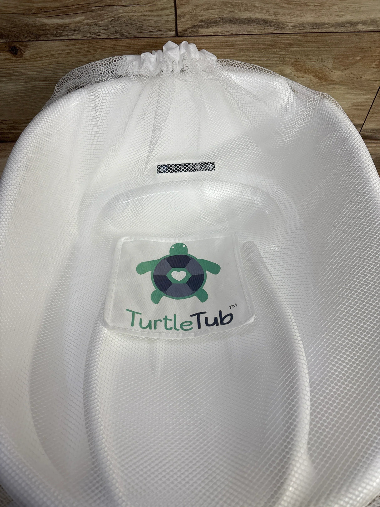 White TurtleTub mesh baby bath seat with turtle logo on wooden floor background