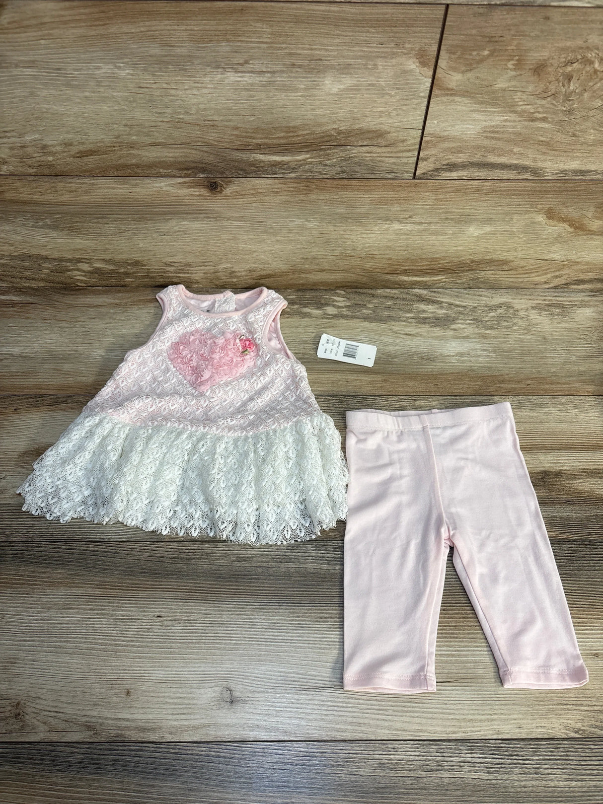 Pink and white lace baby dress with heart detail and matching pink leggings on wood background