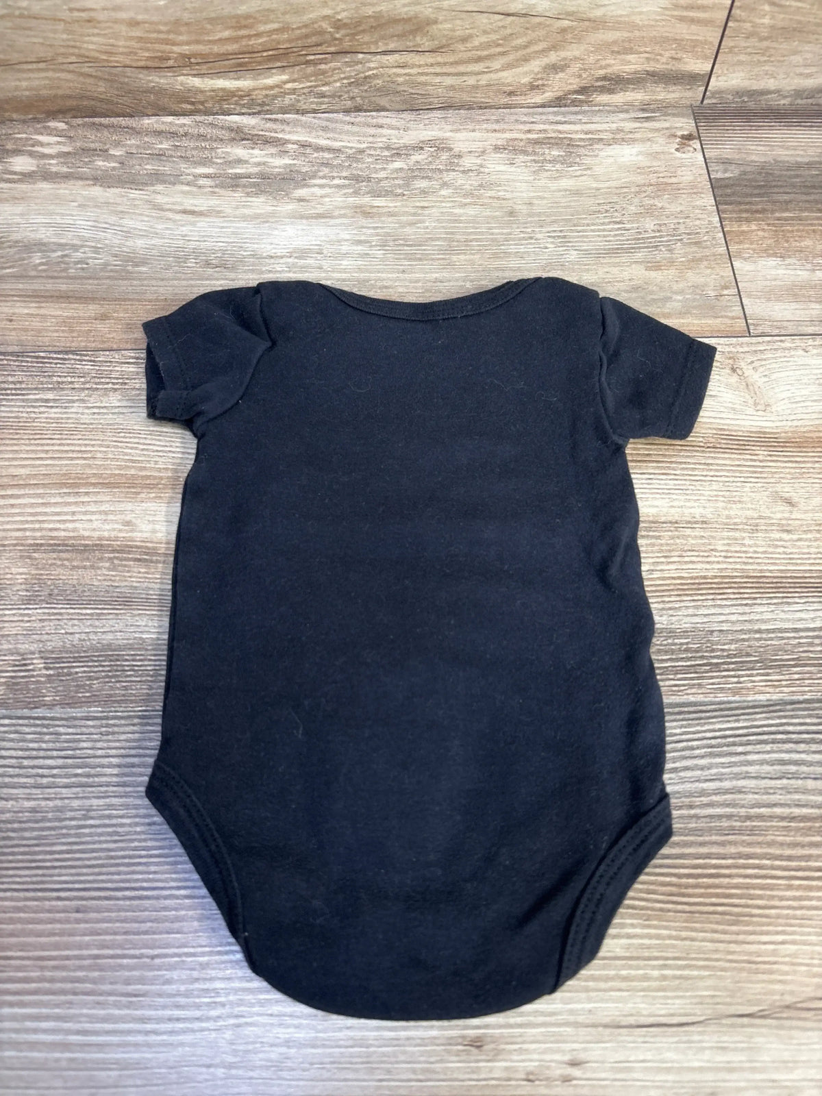 Back flat lay of black baby bodysuit showcasing short sleeves and snap-crotch closure on wood floor background