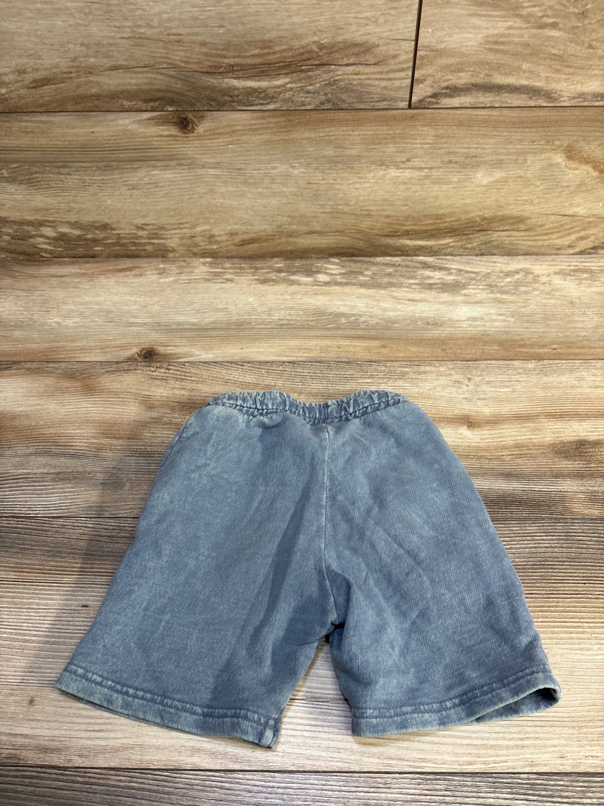 Flat-lay of Tiny Whales blue drawstring toddler shorts showcasing elastic waistband and hem with wooden background