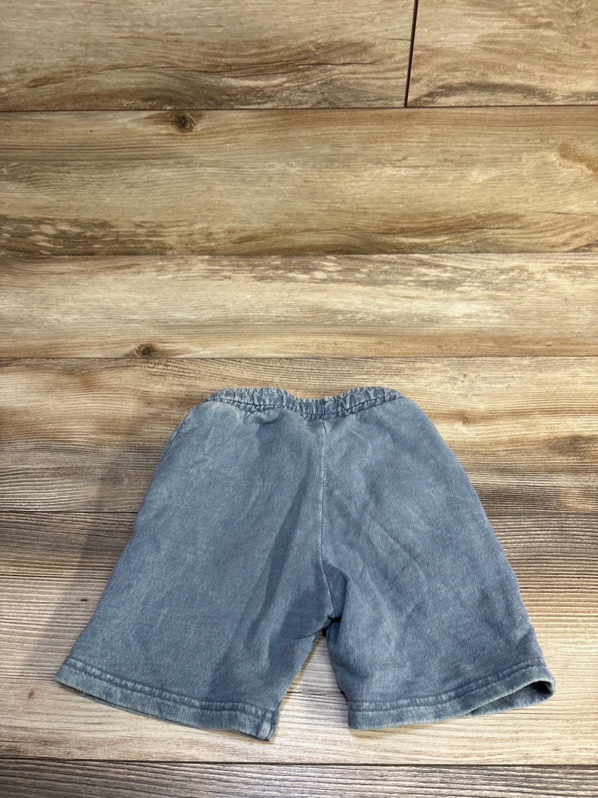 Flat-lay of Tiny Whales blue drawstring toddler shorts showcasing elastic waistband and hem with wooden background