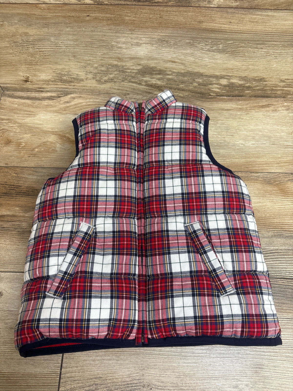 Front view of Janie and Jack reversible tartan puffer vest in red plaid with zip front and pockets on a wood background