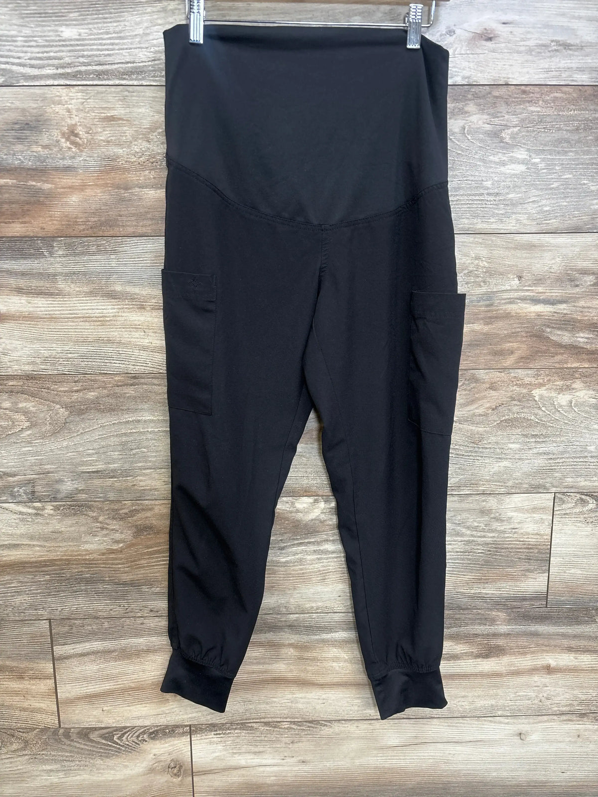 Front view of maternity scrub joggers showing high-rise belly panel, side pockets, and elastic ankle cuffs on wood background
