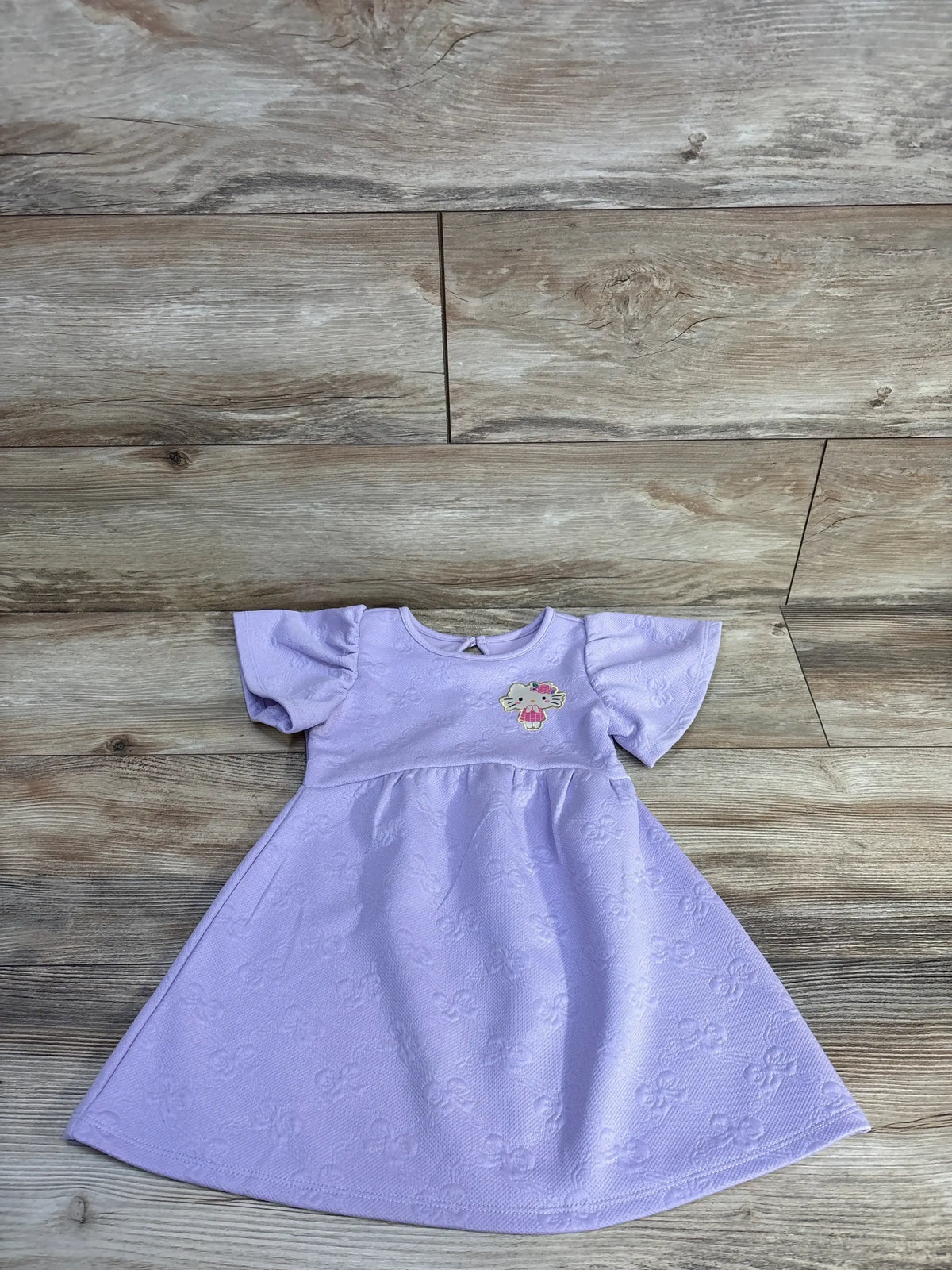Front view of purple Hello Kitty jacquard knit dress with flutter sleeves and embossed pattern on a wood floor