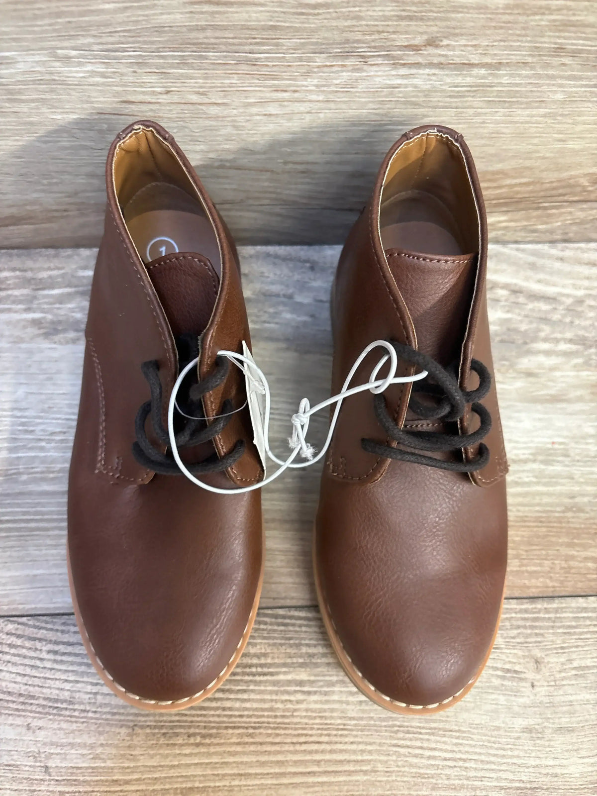 Brown toddler lace-up leather shoes with black laces on wood floor