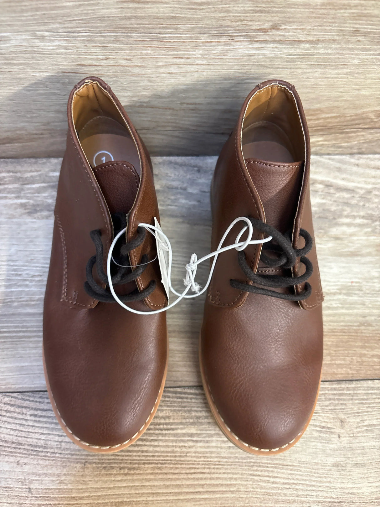 Brown toddler lace-up leather shoes with black laces on wood floor