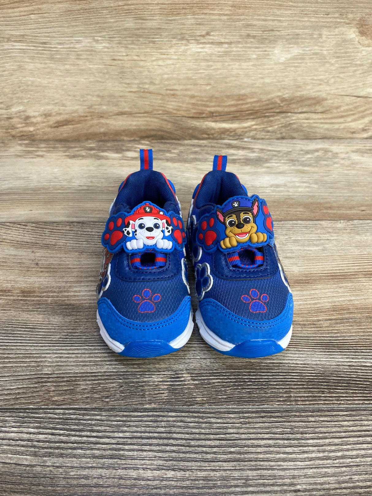 Blue kids sneakers with Paw Patrol characters Marshall and Chase on straps, on wooden floor